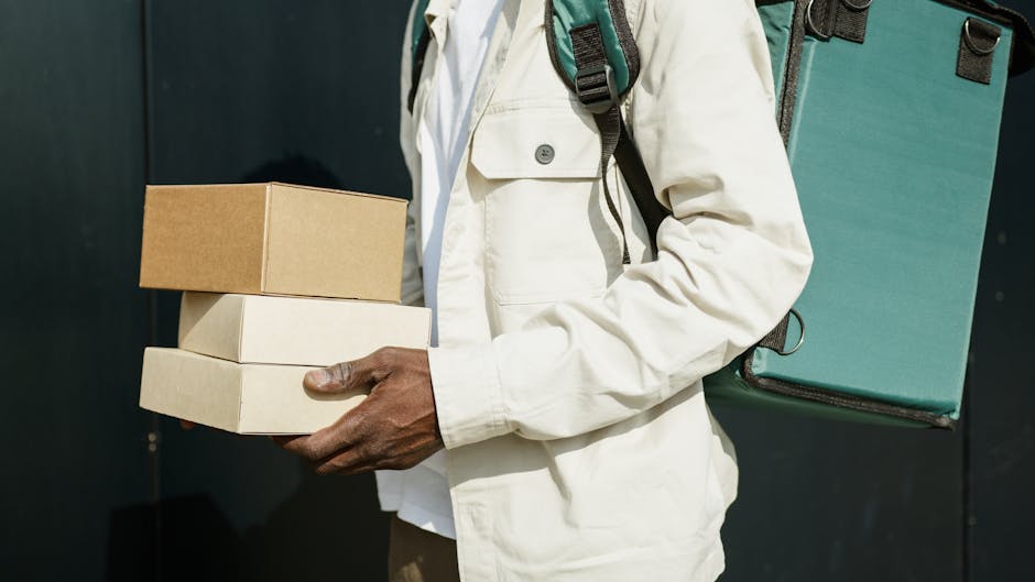 A person wearing a white jacket carrying three stacked cardboard gift boxes in one hand, with a teal backpack on their back. The background is dark and plain. The scene suggests a delivery or gift-giv